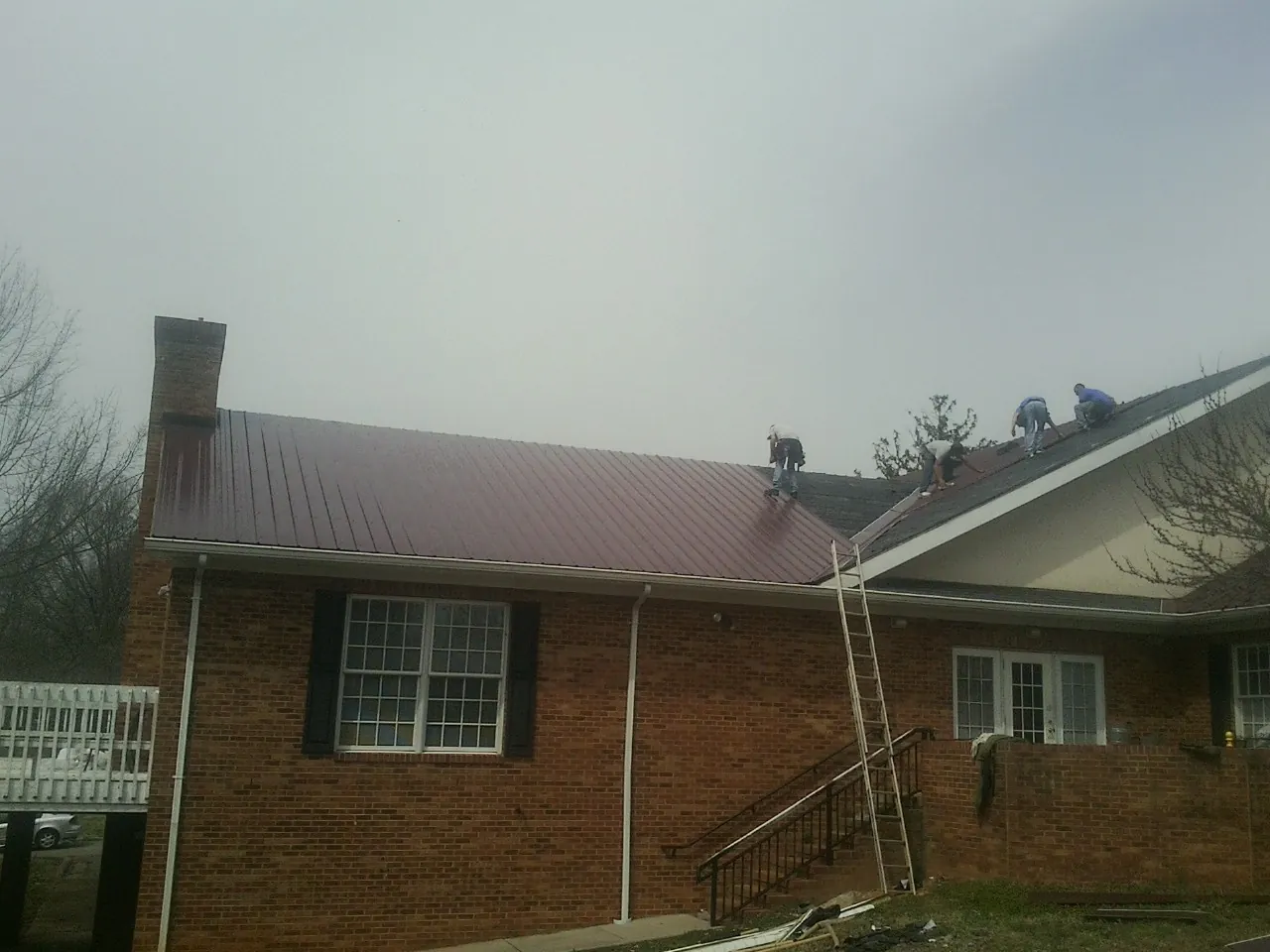 Crew setting red metal roofing panels on a brick home in Somerset